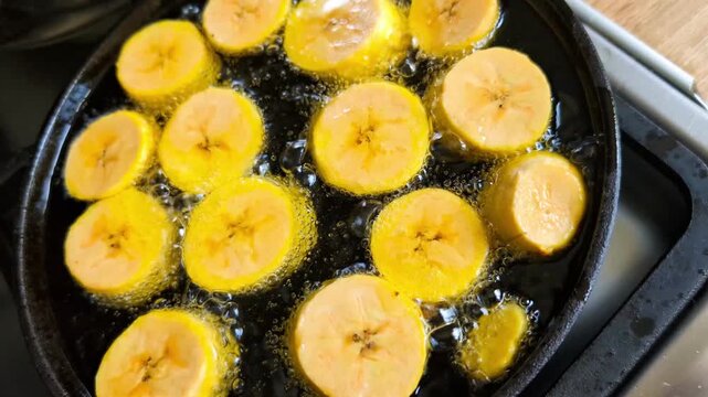 Close up of plantains being deep-fried on black cast iron pan, making patacones