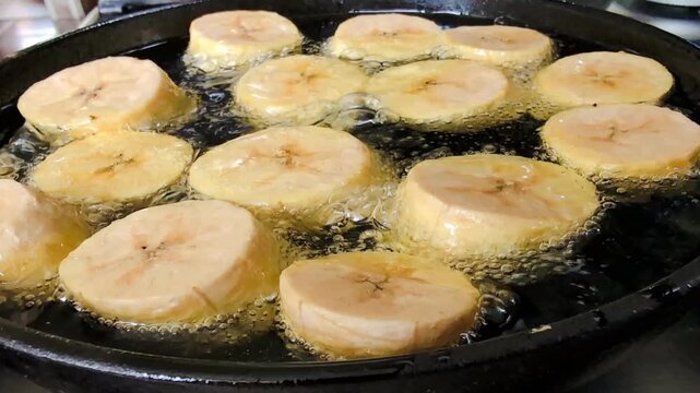 Close up of plantains being deep-fried on black cast iron pan, making patacones