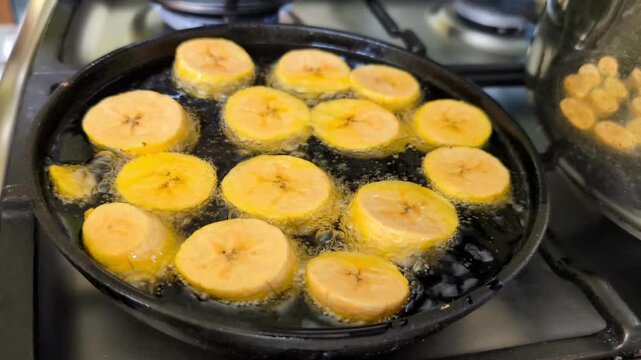 Close up of plantains being deep-fried on black cast iron pan, making patacones
