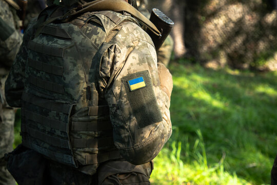 Ukrainian soldier in pixel camouflage uniform with national flag patch sitting in grass