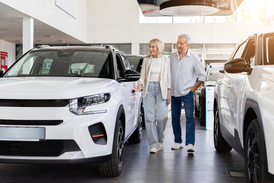 Senior couple walking through modern car dealership showroom while exploring new SUV models and comparing transportation options for future travel needs