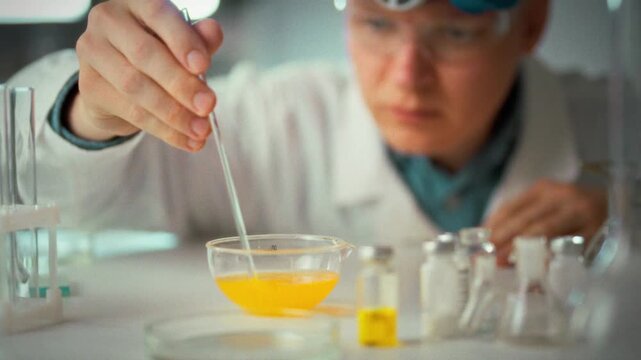 In scientific laboratory, a laboratory assistant wearing protective glasses and a mask conducts an experiment with a bright liquid, emphasizing strict safety measures and precise scientific technique