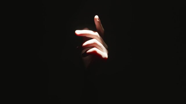 Hand emerging from total darkness into bright spot light