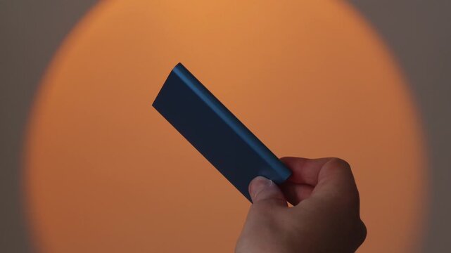 Hand holding slim blue portable SSD on pastel orange background
