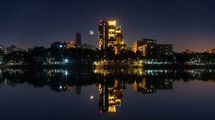 Fototapeta premium Small wooden boat with a glowing lantern floats peacefully on a calm dark lake at night beneath a bright crescent moon while tall city buildings reflect beautifully in the water.