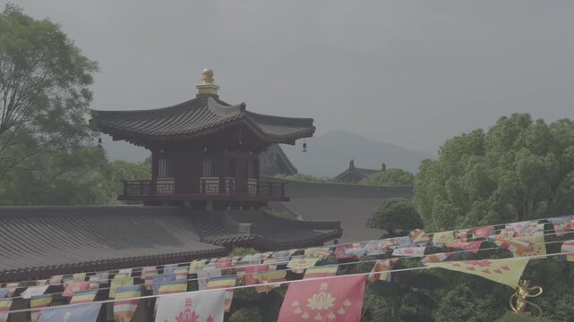 4K resolution static cinematic wide shot of traditional Buddhist prayer flags waving in the wind with ancient wooden temples and misty mountains in the background at Donglin Temple, shot in ProRes Log