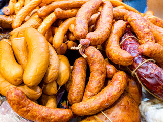 Fototapeta premium Close-up view of assorted smoked and cured sausages arranged in a pile. Different types and textures of sausages are visible, showcasing rich reddish and golden brown colors typical of smoked and drie