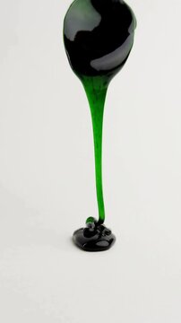 Emerald green liquid dripping on white background, thick viscous fluid pouring in slow motion, glossy translucent slime texture for abstract design