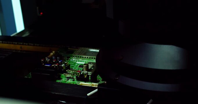 A close-up modern electronic printed circuit board  moving along an automated assembly line conveyor belt inside industrial machinery.Flashing automated optical inspection lights illuminate the board.