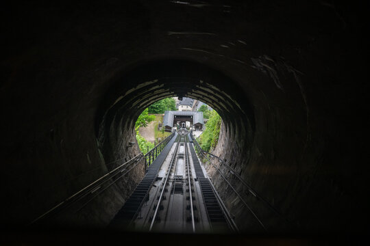View from inside dark tunnel toward hillside funicular station in Salzburg, Austria, with rail tracks and green spring foliage.