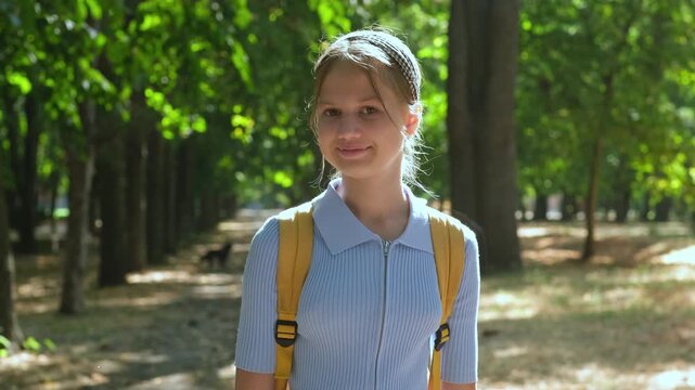 Portrait of cute teenage girl with backpack in bright green park looking at camera. Concept of back to school mood