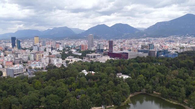 Aerial hyperlapse video tracking dramatic cloud movement above the lush forests of Tirana Grand Park and the tranquil Artificial Lake.