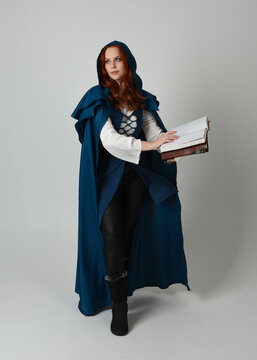 full length portrait of female model wearing medieval fantasy warrior historical costume with blue cloak. silhouette figure,  holding magical spell book on studio background.

