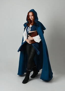 full length portrait of female model wearing medieval fantasy warrior historical costume with blue cloak. silhouette figure,  holding magical spell book on studio background.
