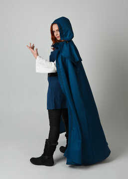 full length portrait of model wearing medieval fantasy warrior historical costume with blue hooded cloak. silhouette figure,  walking away in back view on studio background.