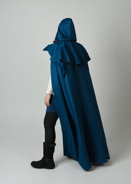 full length portrait of model wearing medieval fantasy warrior historical costume with blue hooded cloak. silhouette figure,  walking away in back view on studio background.