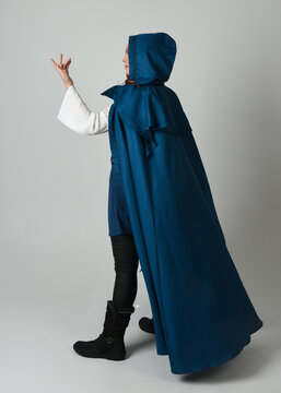 full length portrait of model wearing medieval fantasy warrior historical costume with blue hooded cloak. silhouette figure,  walking away in back view on studio background.