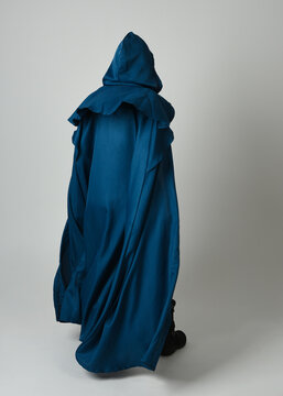 full length portrait of model wearing medieval fantasy warrior historical costume with blue hooded cloak. silhouette figure,  walking away in back view on studio background.