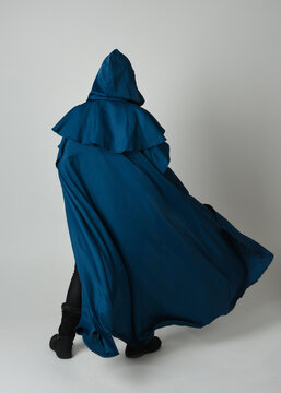 full length portrait of model wearing medieval fantasy warrior historical costume with blue hooded cloak. silhouette figure,  walking away in back view on studio background.