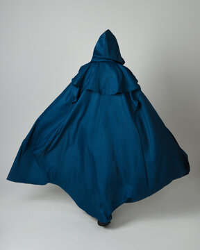 full length portrait of model wearing medieval fantasy warrior historical costume with blue hooded cloak. silhouette figure,  walking away in back view on studio background.