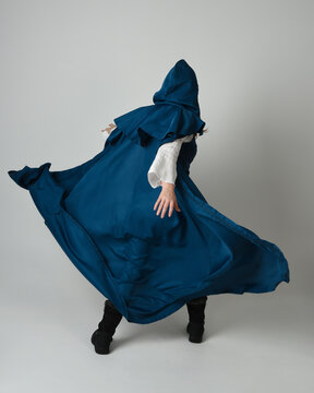 full length portrait of model wearing medieval fantasy warrior historical costume with blue hooded cloak. silhouette figure,  walking away in back view on studio background.