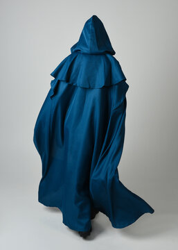 full length portrait of model wearing medieval fantasy warrior historical costume with blue hooded cloak. silhouette figure,  walking away in back view on studio background.