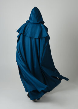 full length portrait of model wearing medieval fantasy warrior historical costume with blue hooded cloak. silhouette figure,  walking away in back view on studio background.