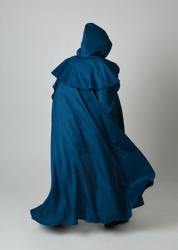 full length portrait of model wearing medieval fantasy warrior historical costume with blue hooded cloak. silhouette figure,  walking away in back view on studio background.