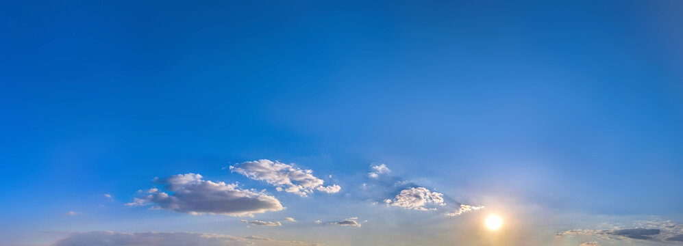 Expansive sky where a low sun gilds scattered clouds, blue deepening toward zenith softening along horizon. Subtle halos delicate contrasts between light shadow convey sense open air quiet movement.
