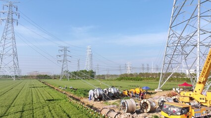 Construction scene with power line towers and workers under high voltage transmission lines in a green field © zhu difeng
