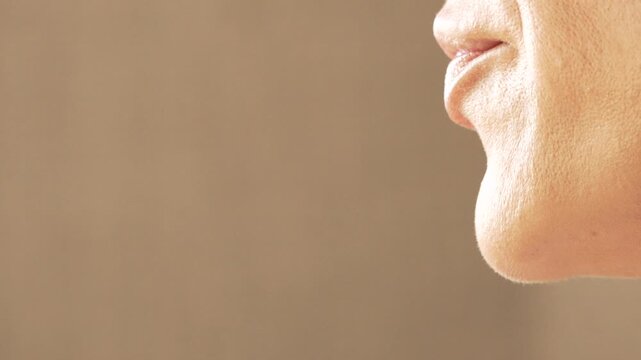 Mouth, lips, woman speaking, close-up. A beauty professional applies foundation with a brush to the chin and jawline of a female model.