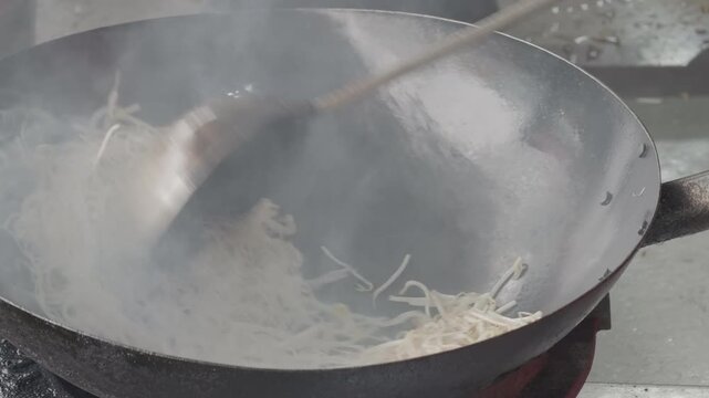 Close up of chef stir-frying noodles with bean sprouts in a hot smoking wok, traditional Asian street food cooking