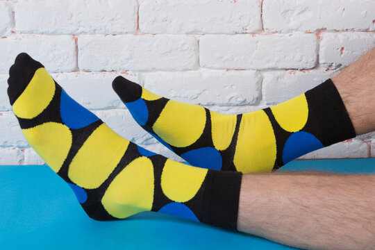 Male legs wearing funny bright yellow and blue patterned socks resting on a blue surface against white brick wall