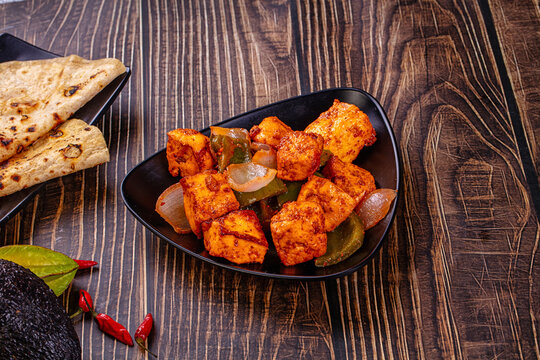Indian Paneer Tikka Masala inl with Roti bread on a dark wooden table