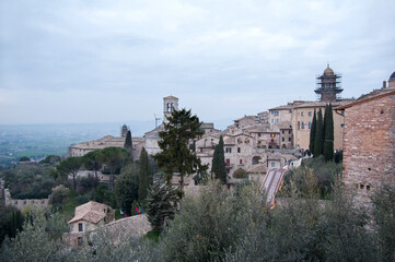 Naklejka premium View of the Assisi village on the slopes of Mount Subasio with the Spoleto (Umbro) Valley below at sunset. Umbria, Italy