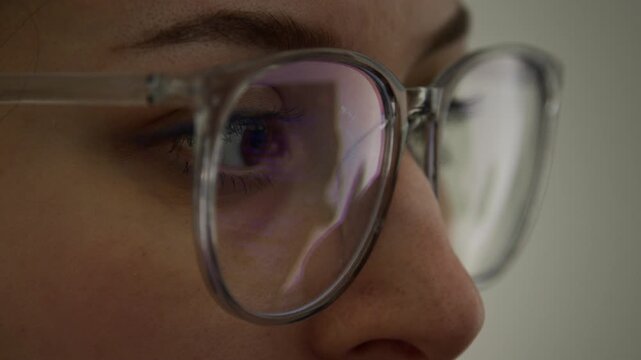 Extreme close-up of eyes of young Caucasian female programmer or software developer, wearing eyeglasses, staring at computer screen while working on code