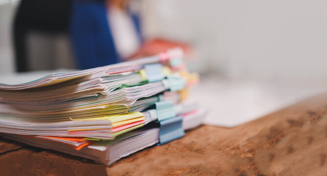 Stacked office document papers with an assortment of colorful binder clips on a rustic wooden desk, indicating organization strategy, managing files, and processing important information