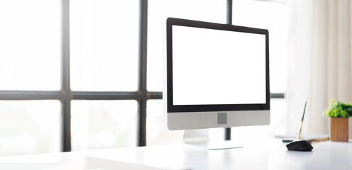 Fototapeta premium Modern computer display with a blank white screen on a sleek desk, providing ample copy space for creative mockups, showcasing a bright and minimalist workplace