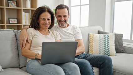 Fototapeta premium Mature couple enjoys viewing content on laptop while seated together on sofa at home