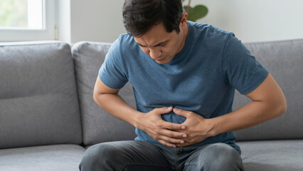 Obraz premium Man with Stomach Ache on Sofa at Home – Concerned Mature Male in Casual Wear for Health Blogs, Travel Sickness Concepts, and Medical Illustration