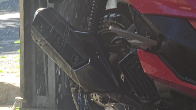 High pressure water spraying on the lower section and exhaust pipe of a red motorcycle during a cleaning process