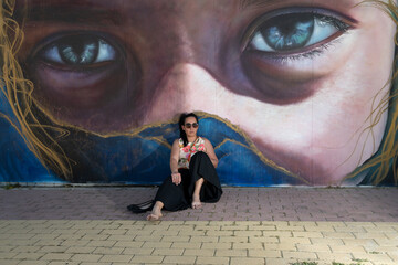 Woman sitting by mural with giant eyes gazing © Mandy