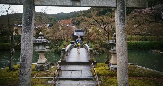 Little boy fast walking under stone torii gate and across wet bridge - wide, steady cam shot