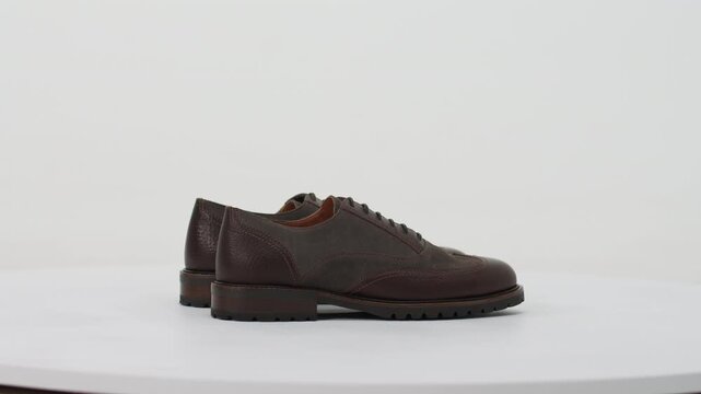 Elegant brown leather and suede brogue shoes for men rotating on a turntable isolated on a white background