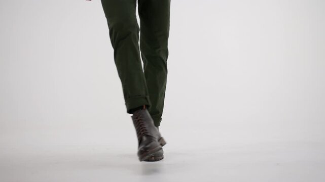 Person walking, dancing, and twisting in brown leather boots and green pants isolated on a white background