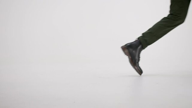Man wearing combat boots and green pants walking from left to right isolated on a white background, side view close-up