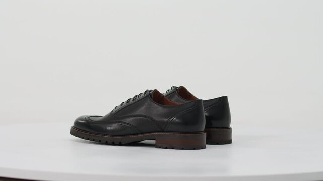 Black leather derby shoes with brogue details rotating on a turntable isolated on a white background