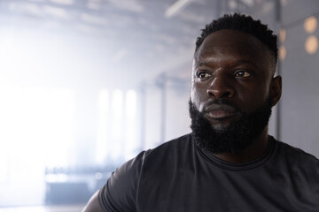 Obraz premium African American adult man training in gym wearing fitted dark tee, equipment blurred, copy space