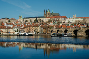 Fototapeta premium Discover the stunning beauty of Pragues riverfront and historic skyline under a clear blue sky