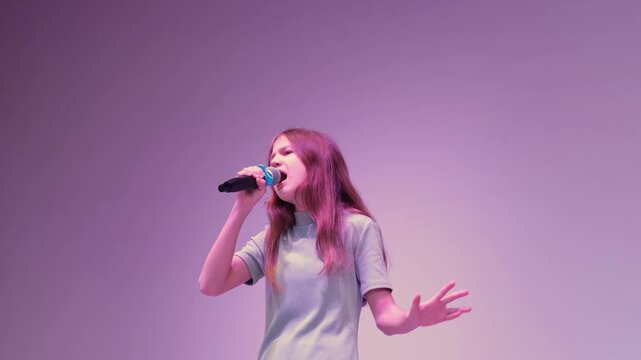 Preteen girl with microphone singing song on stage in purple light. Vocal training and singing competition concept